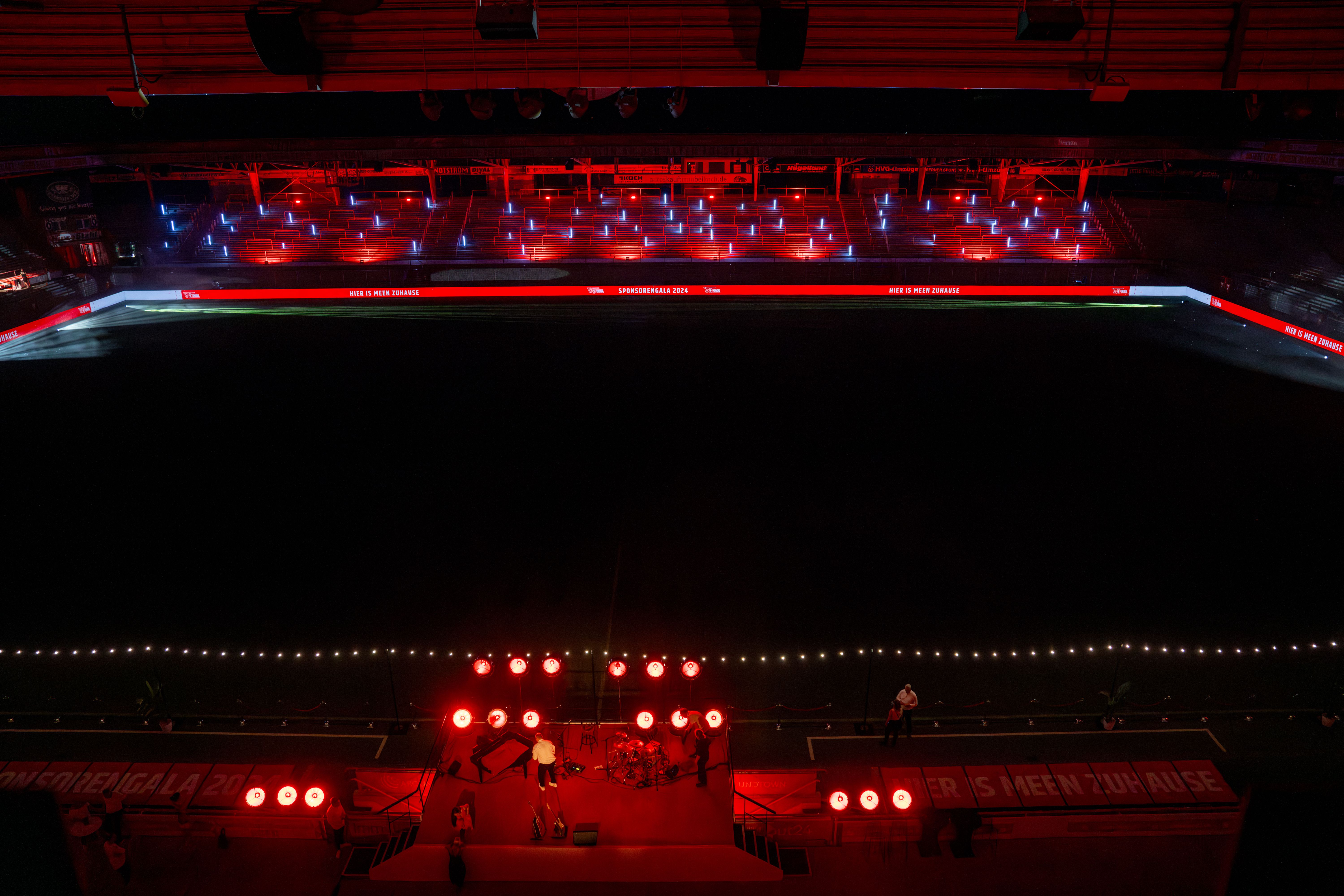 View of an empty football field, illuminated by red and green lights, with a stage in the foreground.