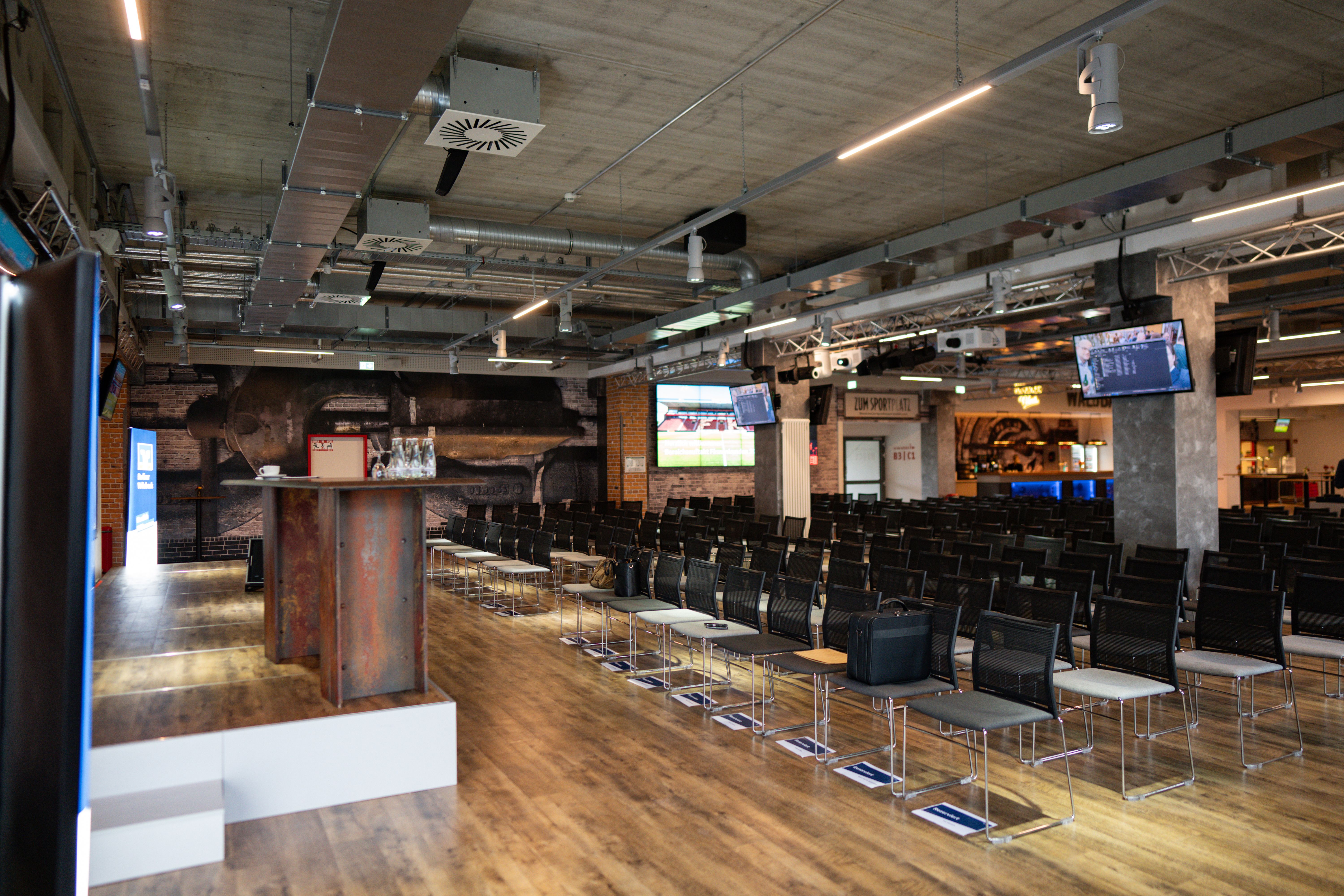 Leerer Konferenzraum mit Reihen von Stühlen, Präsentationsbildschirmen und einer Theke im Vordergrund.