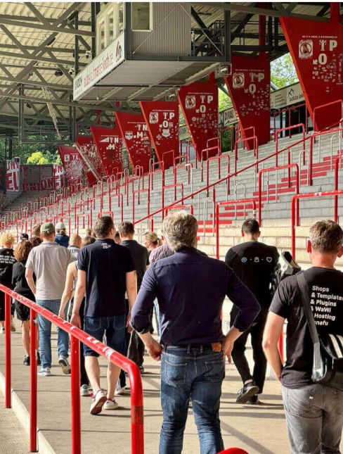 Menschen gehen eine Treppe hinunter in ein Stadion mit roten Sitzen und Fahnen.