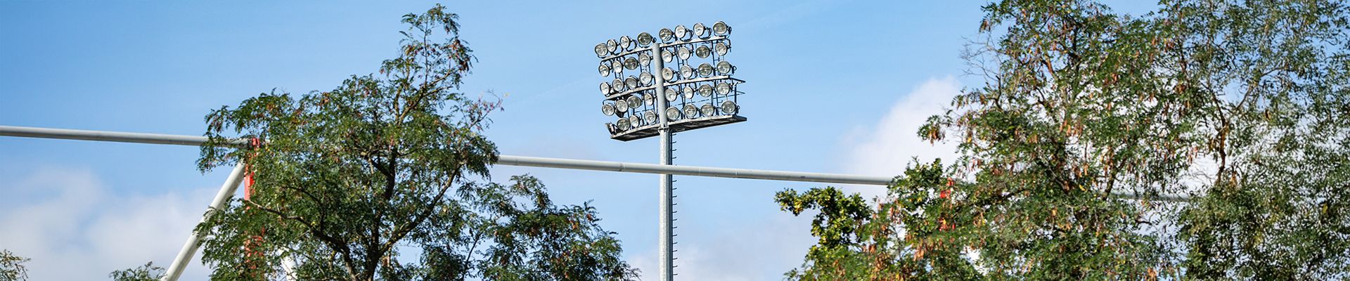 Flutlichtmast über Bäumen unter einem blauen Himmel.