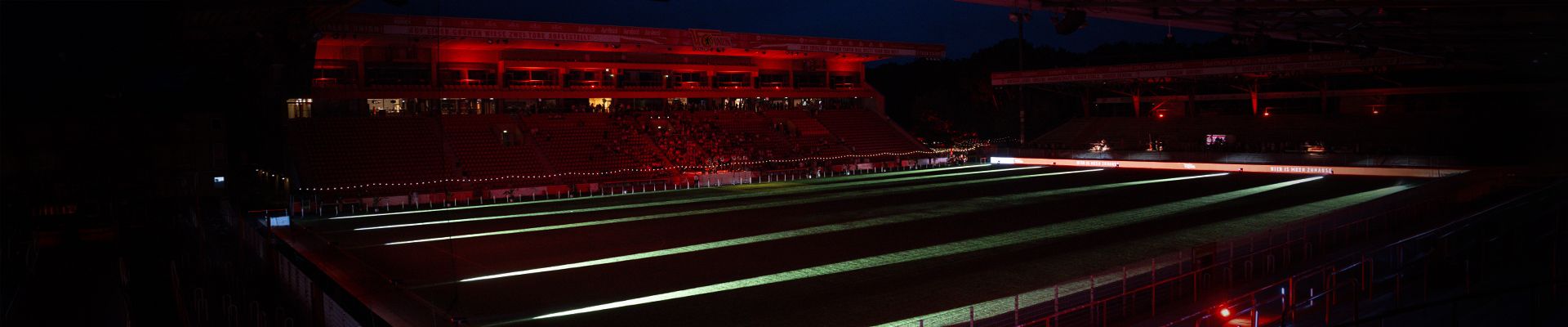 Ein beleuchtetes Sportstadion bei Nacht mit roten Lichtern und leeren Tribünen.