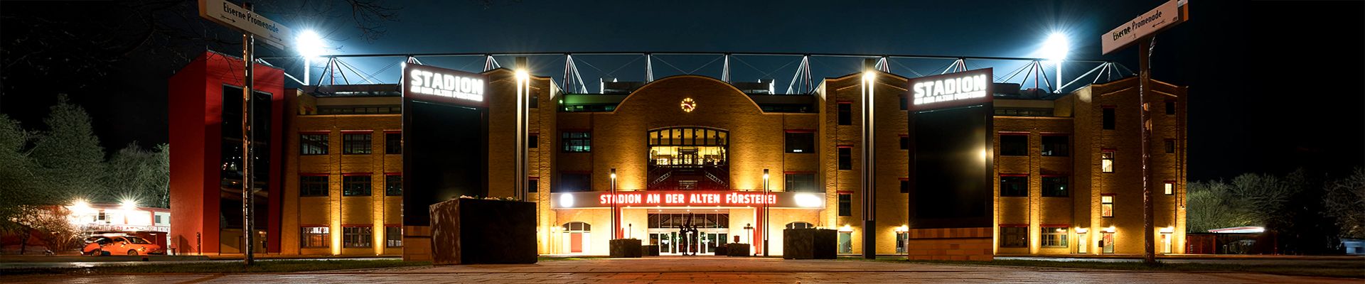 Stadion mit beleuchteter Fassade bei Nacht, auffällige Schilder und Lichter auf dem Dach.